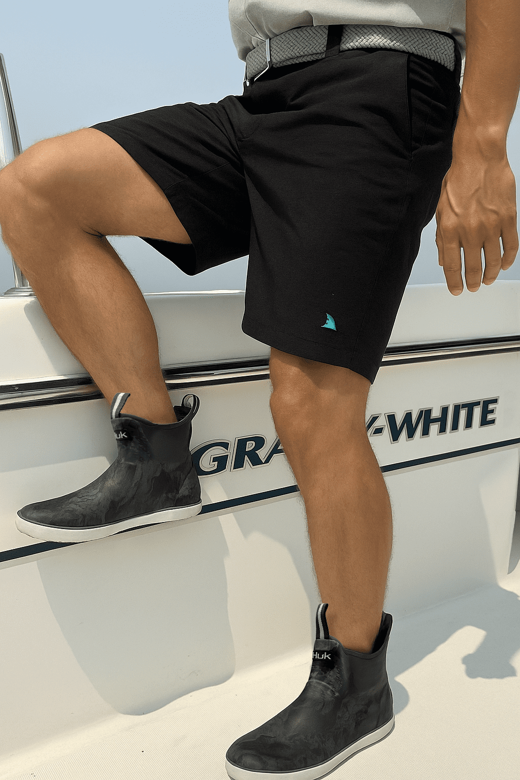 Man climbing onto his Grady White boat wearing HUK boots and Black Hybrid Bay Shorts by Made In Dade