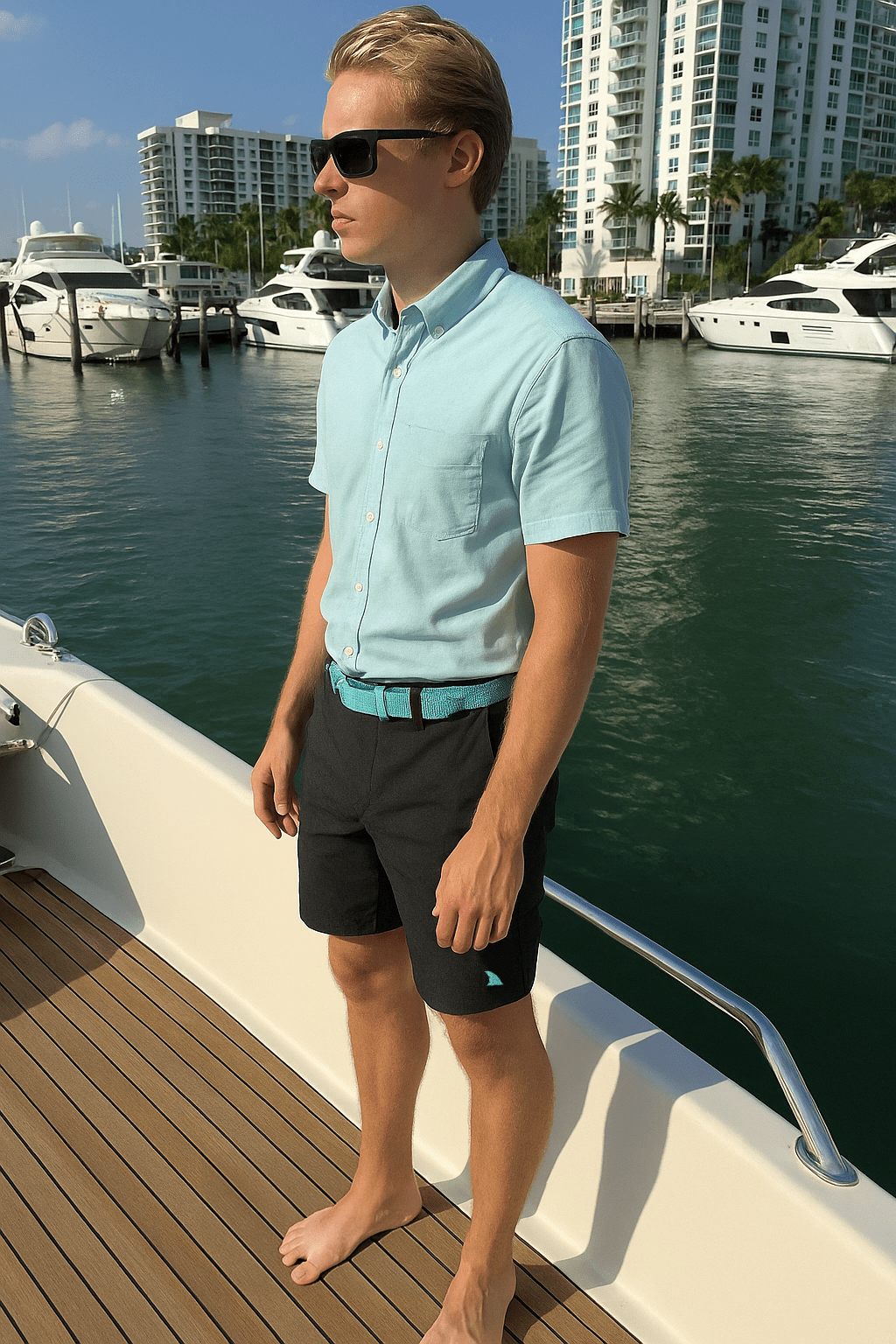 Barefooted Young blonde man on the stern deck of a private Yacht wearing Black Heather Hybrid Bay Shorts by Made In Dade